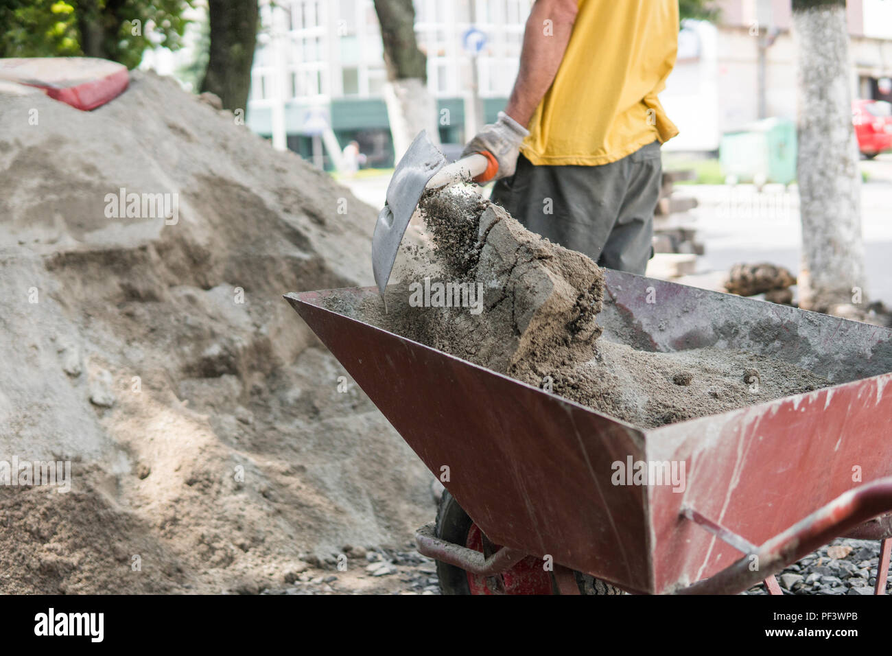 Worker use the shovel and fill the wheelbarrow with sand for construction of sidewalk road