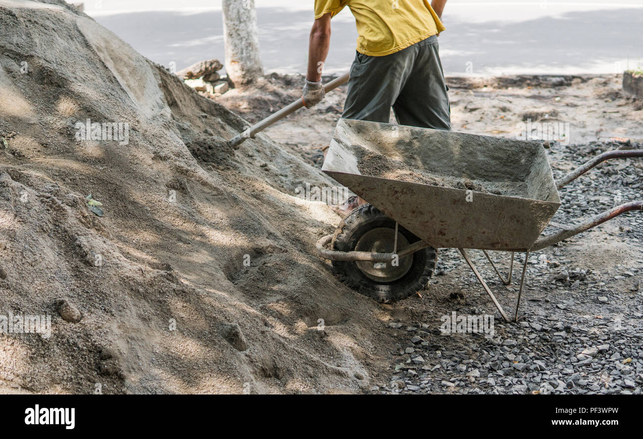 Worker use the shovel and fill the wheelbarrow with sand for construction of sidewalk road