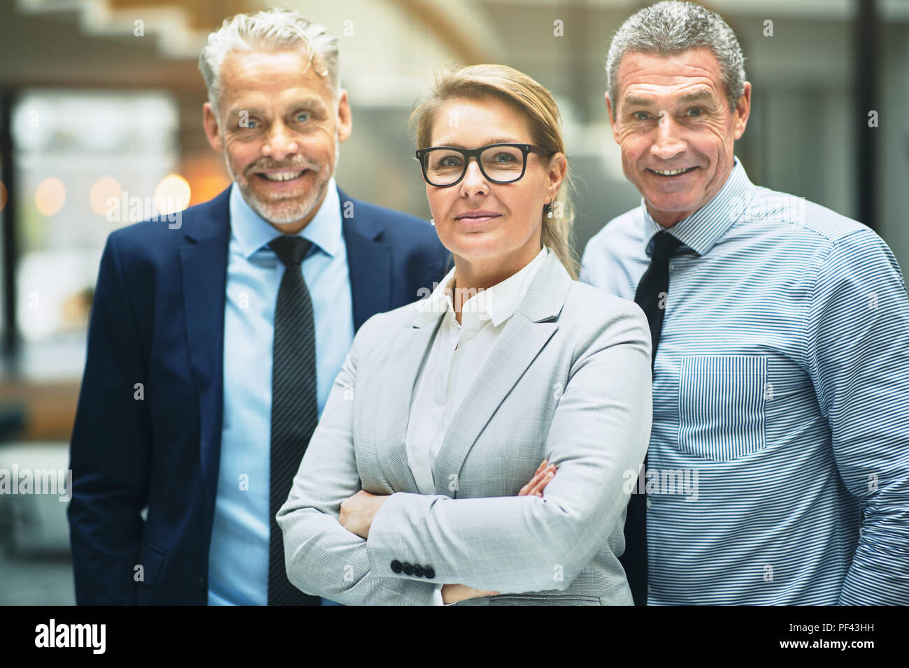Group of smiling mature corporate colleagues standing confidently together in the lobby of a modern office building Stock Photo
