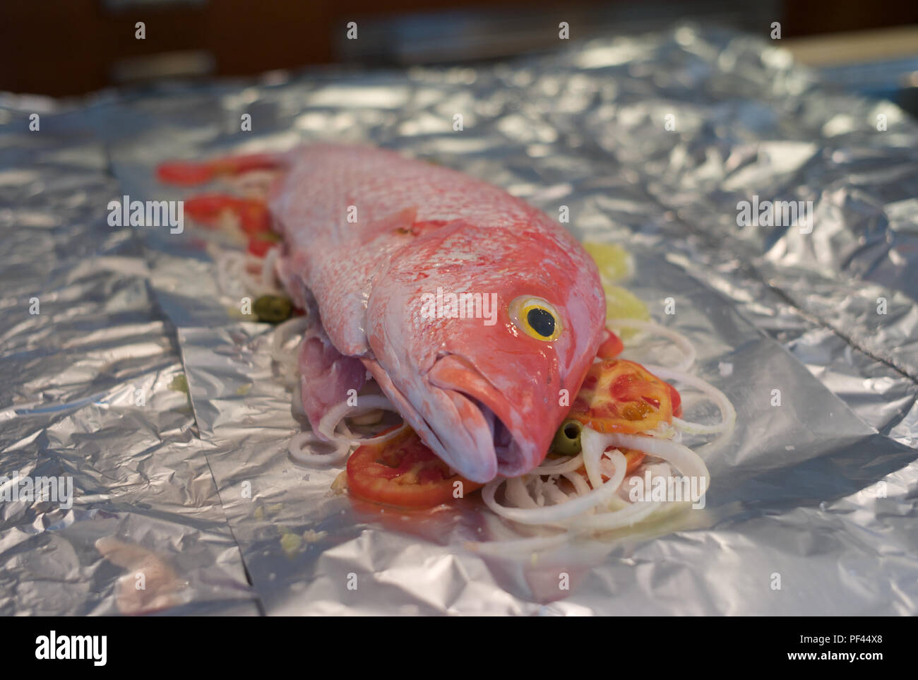 Cooking Red Snapper - Raw red fish on tomatoes, olives and onions, placed on tin foil Stock Photo
