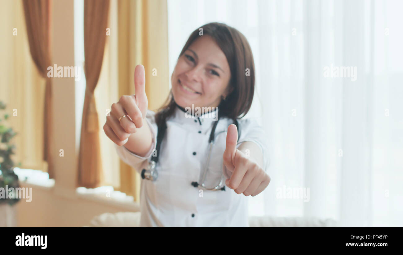 Portrait of a young female doctor in a good mood who shows thumbs up. Stock Photo