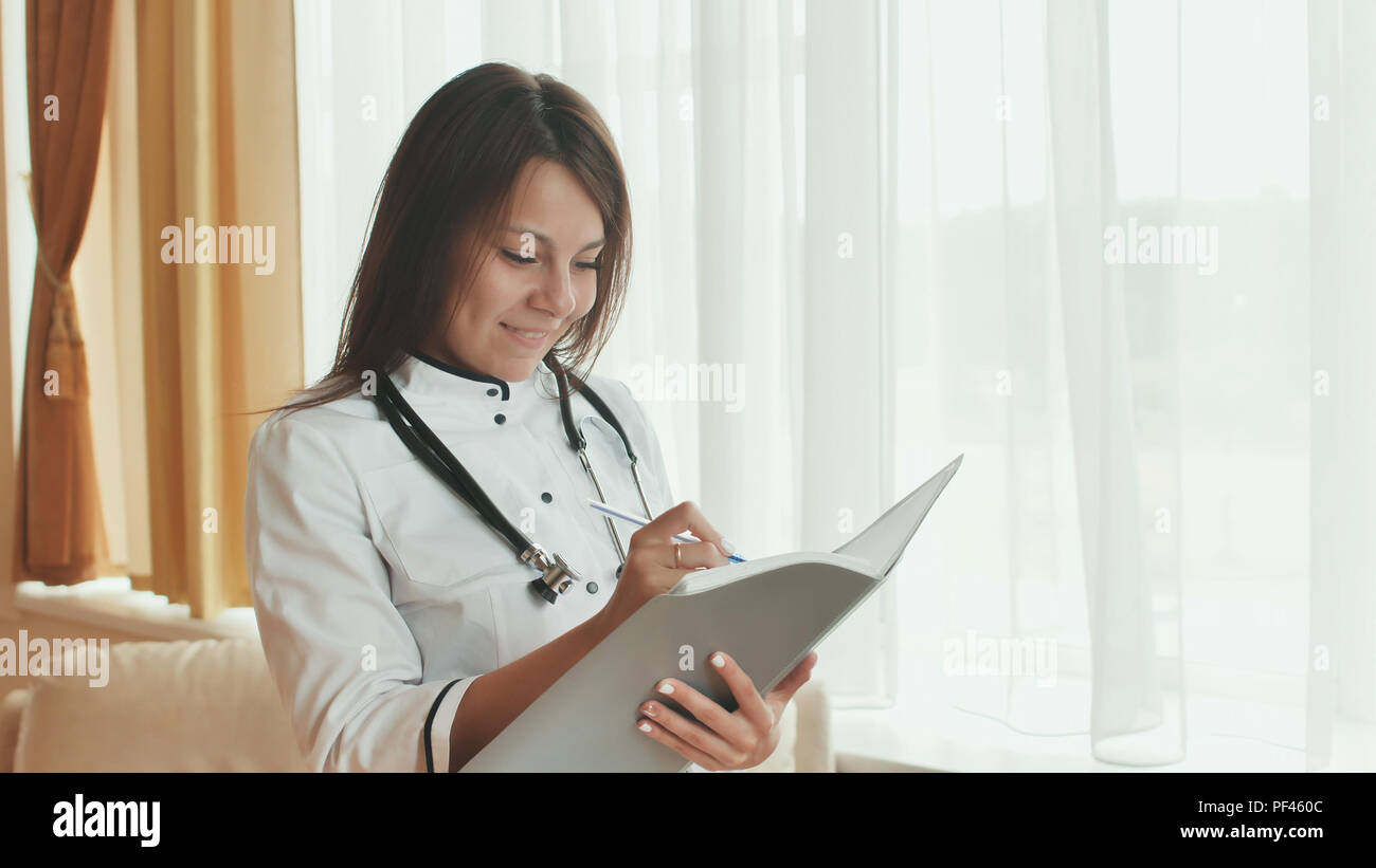 A young woman doctor writes in a summary in a good mood. Stock Photo