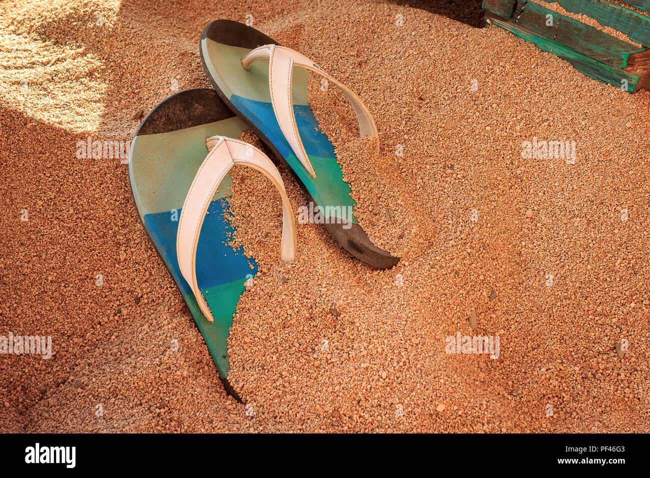 Colorful flip-flops on a golden, fine sand on a beach in a bar with wooden furniture Stock Photo