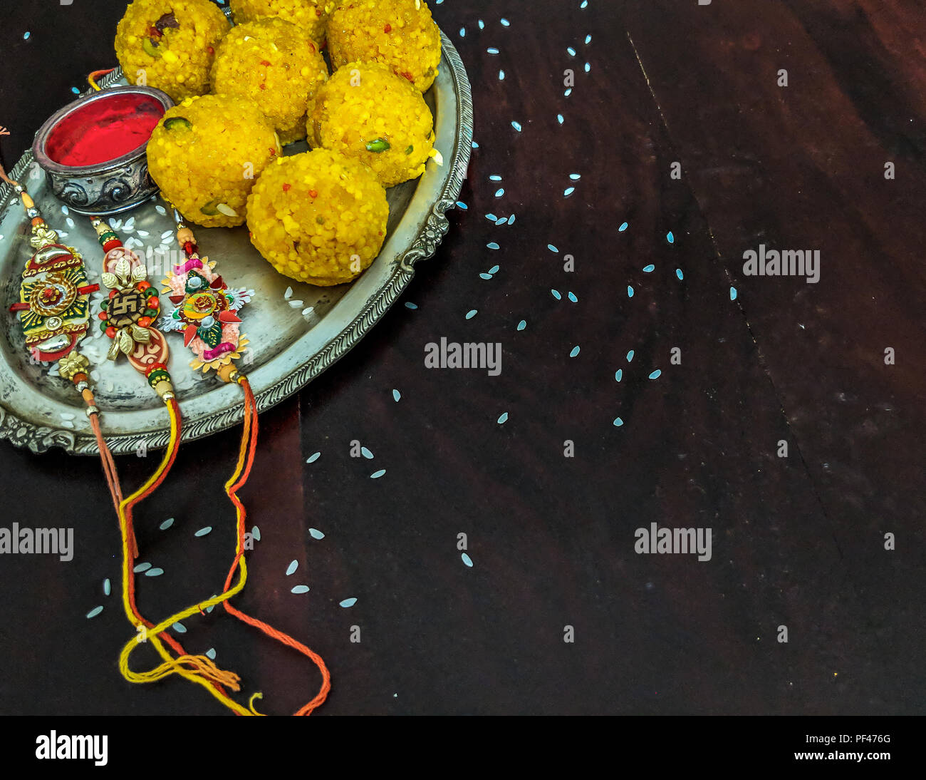 Rakhi with rice grains, kumkum and sweets on decorative plate and background with elegant Rakhi. A traditional Indian wrist band, symbol of love betwe Stock Photo