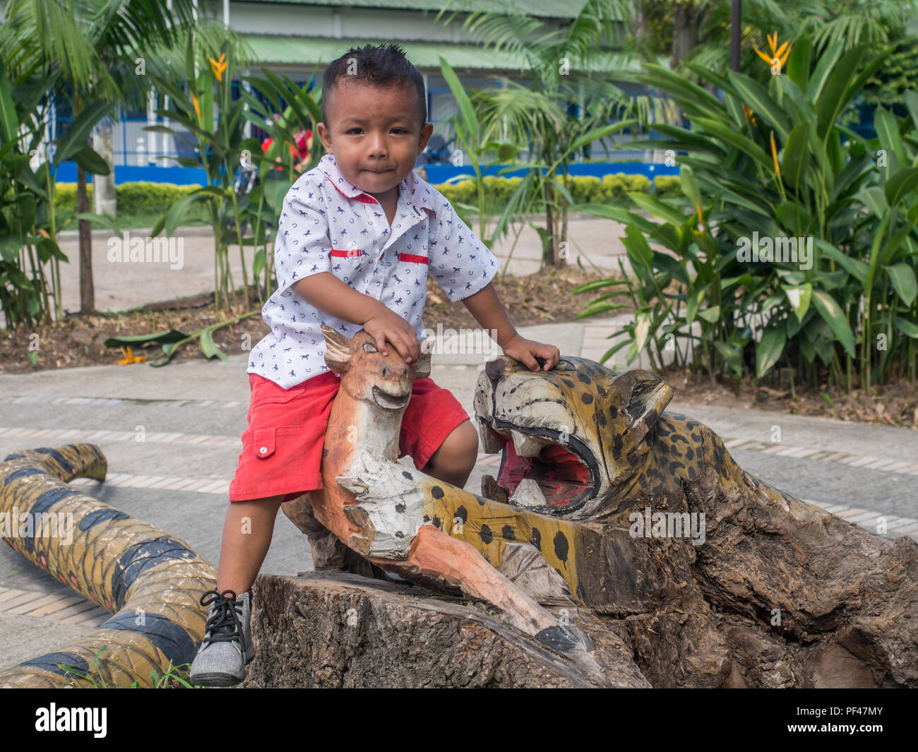 Leticia, Colombia  - March 03, 2018: Small colombian boy sitting on the wooden animal in the small village in Colombia Stock Photo