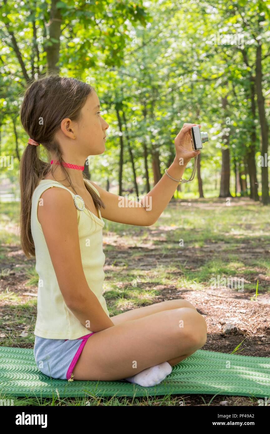 Little girl child of 8 years looking at camera sitting on green lawn in  city park. girl 8 years in the park taking pictures of nature. vertical  photo Stock Photo - Alamy
