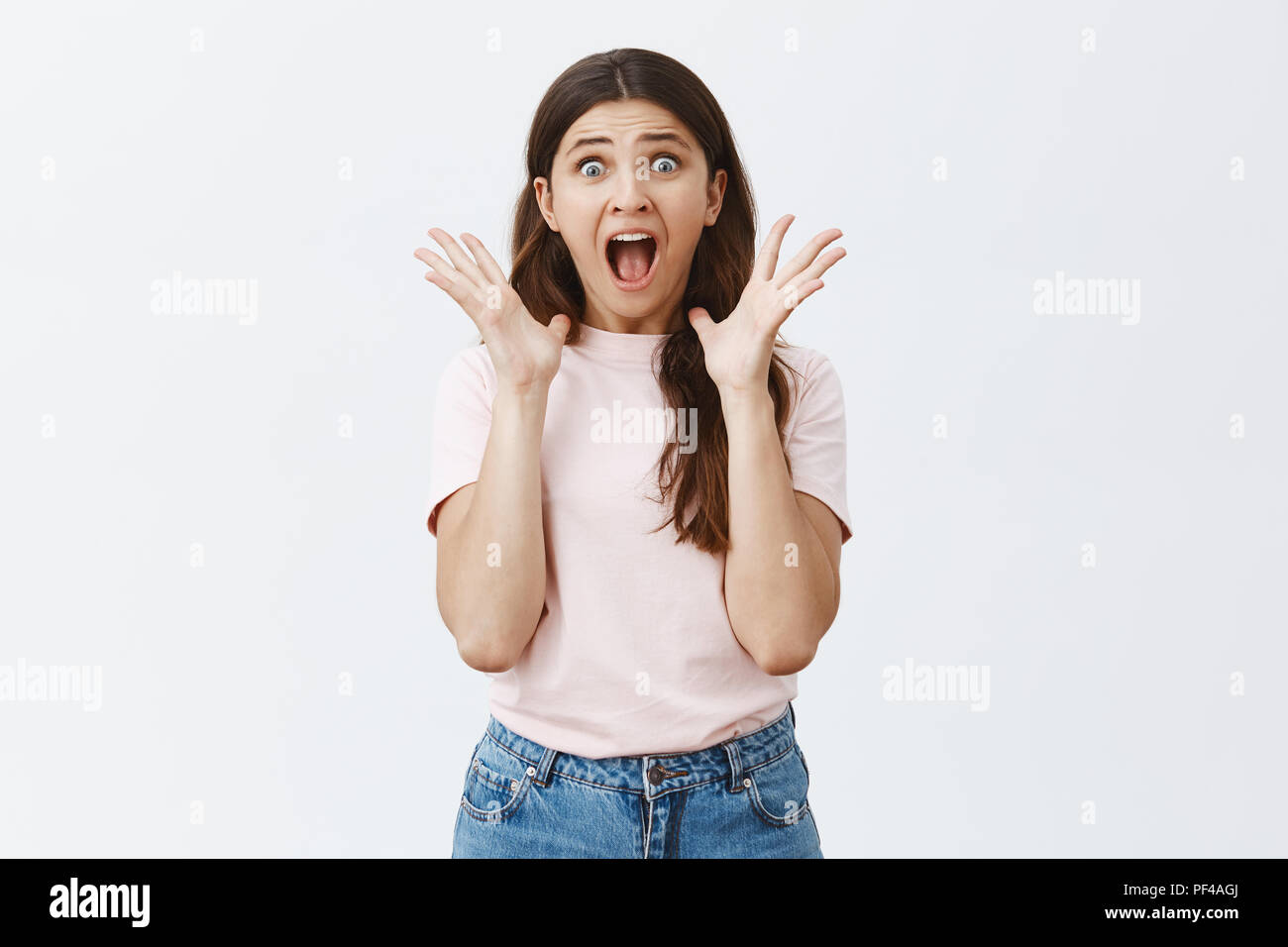 Woman yelling from fear out loud so neighbors woke up. Shocked girl screaming for help popping eyes and staring at camera with frightened expression raising palms near face and opening mouth Stock Photo
