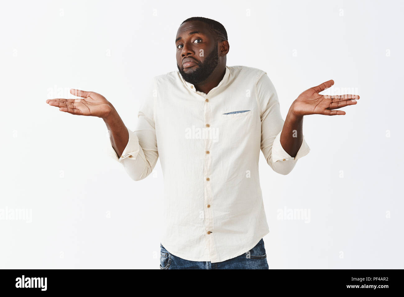 Bro have no idea. Portrait of clueless handsome African American in white shirt and jeans, shrugging with both hands aside, pursing lips and pouting, being unaware and uncertain in answer Stock Photo