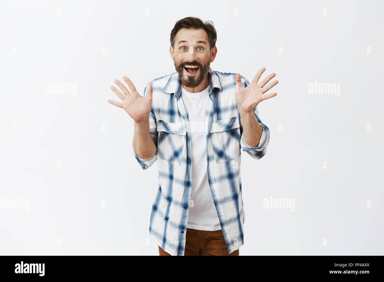 Jazz hands make day happier. Portrait of charming excited joyful european male with beard and moustache, waving raised palms, stooping and smiling joyfully, standing over gray background amused Stock Photo