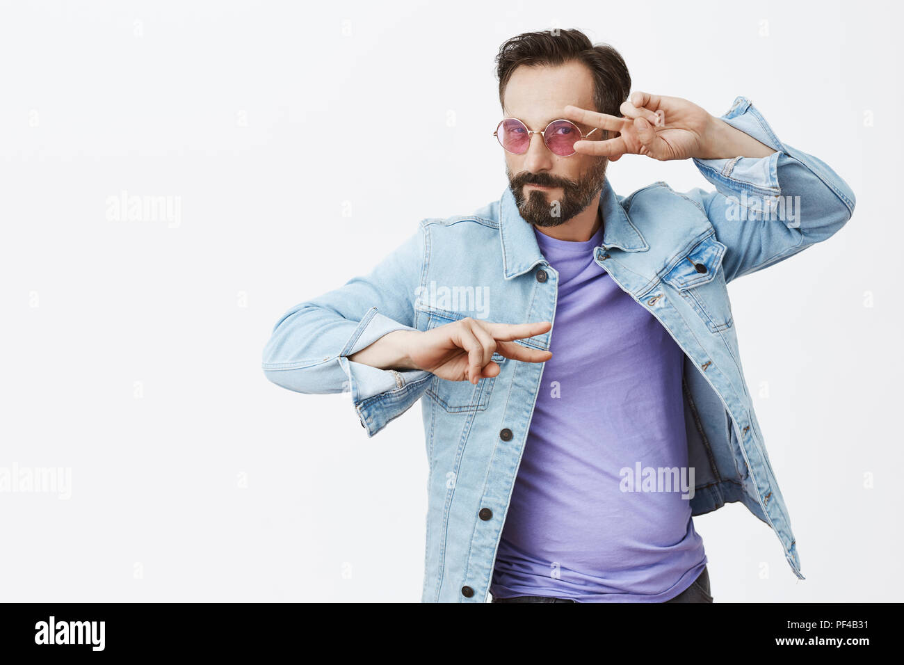 Let us lit this dancefloor. Charming flirty and emotional good-looking male in denim jacket and stylish sunglasses, dancing and making disco gesture or peace signs over eyes, looking at camera Stock Photo
