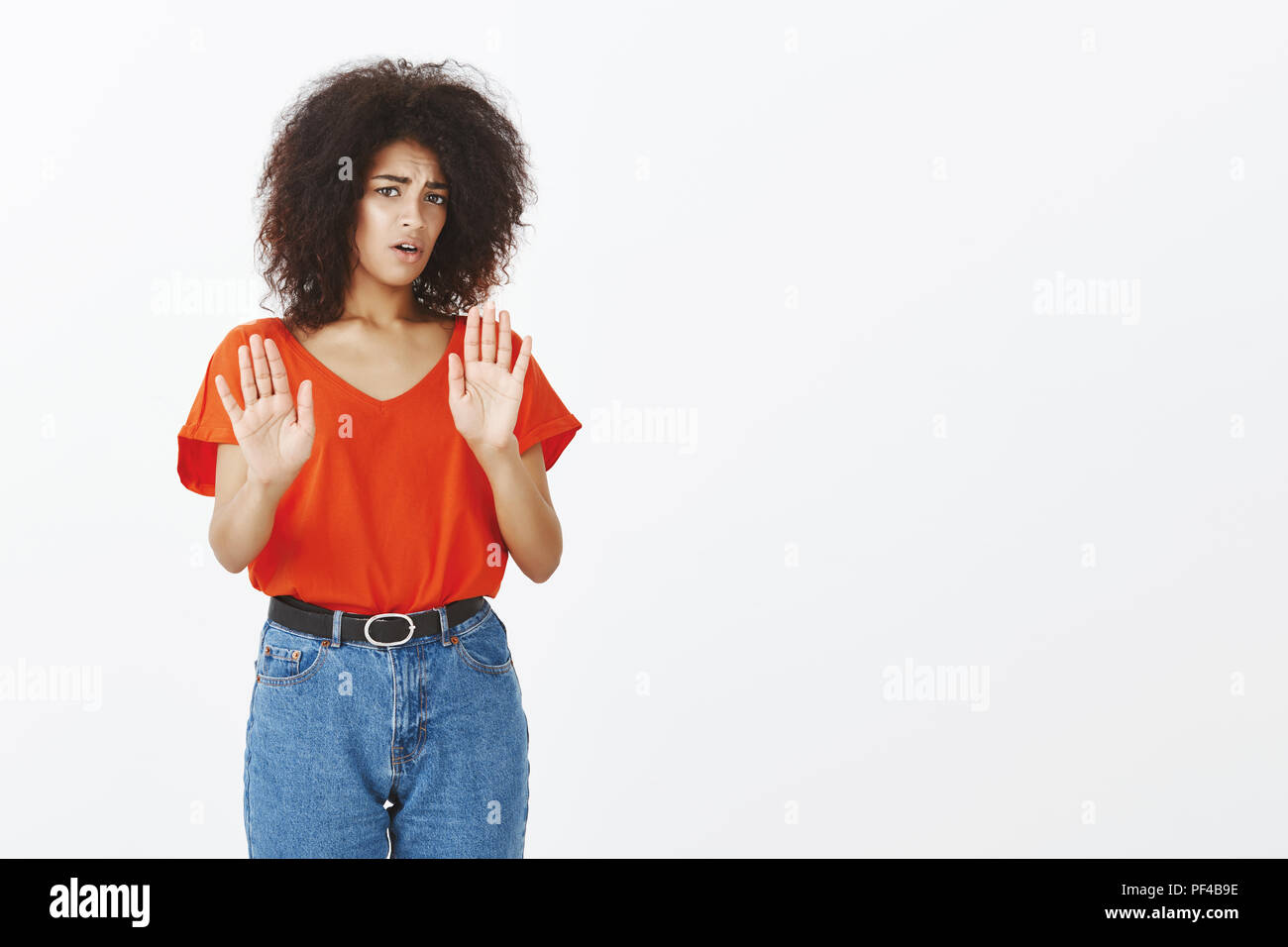 No thanks. Displeased attractive stylish woman with dark skin and curly hair, pulling hands in stop or enough gesture, expressing rejection and antipathy while standing over gray background Stock Photo