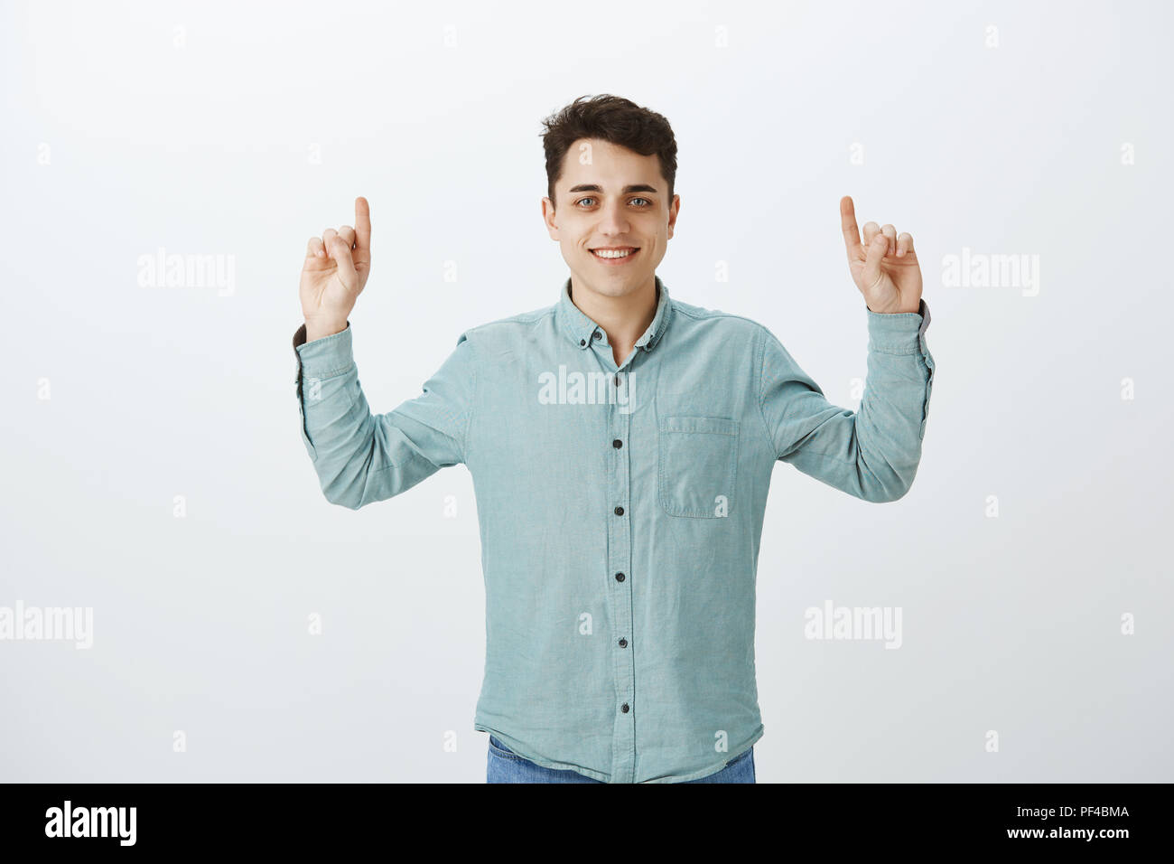 Portrait of carefree good-looking young man in casual outfit, raising index fingers and pointing up, smiling broadly, sharing great place for advertisement or giving directions to stranger on street Stock Photo