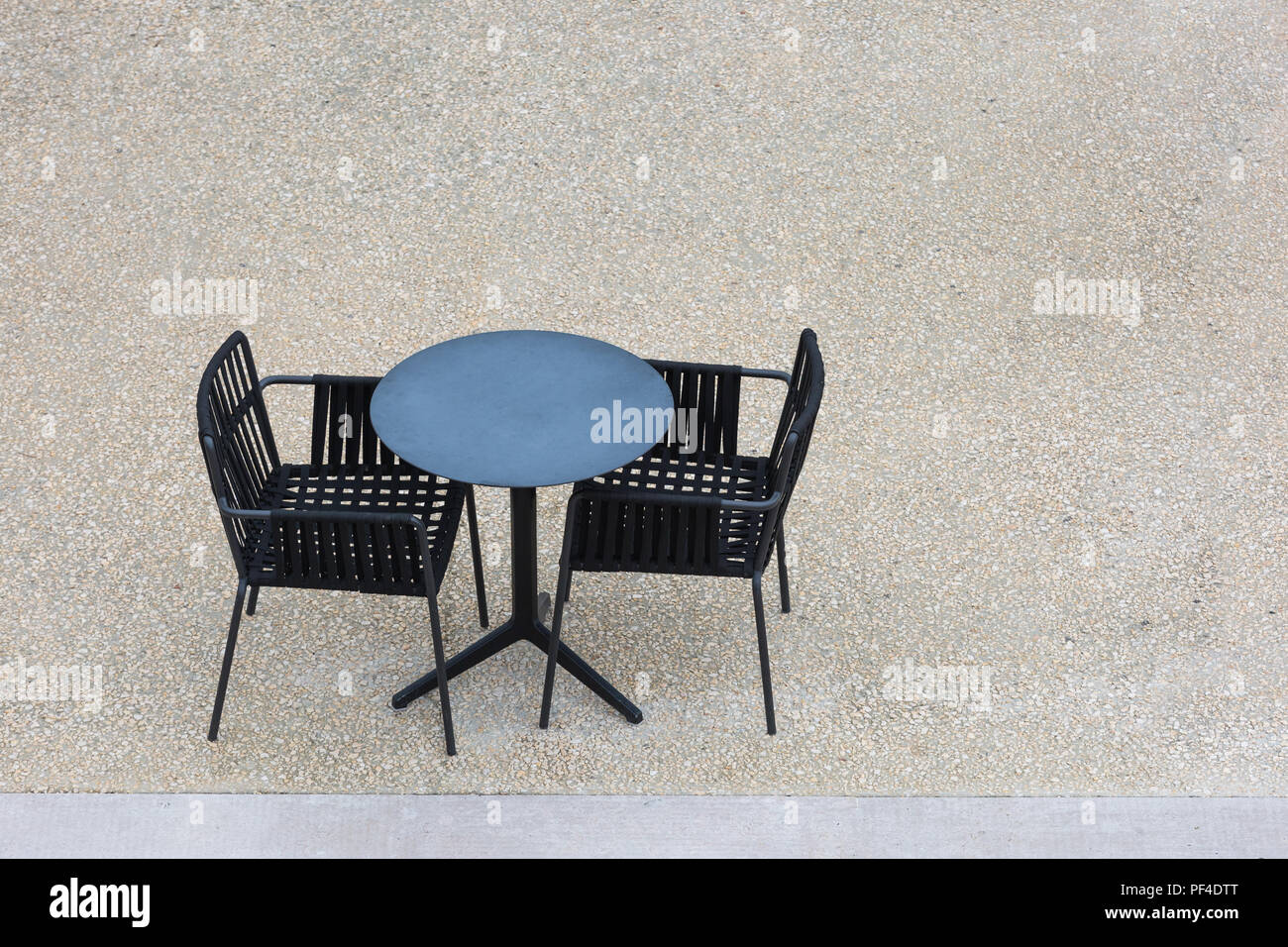 Two empty black chairs and a table on concrete from above Stock Photo