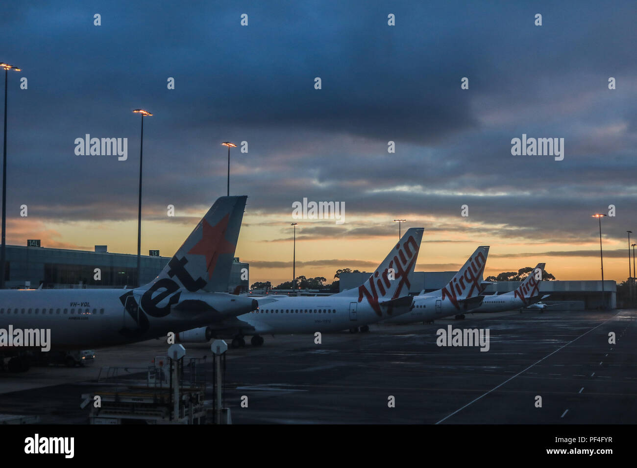 Adelaide, Australia. 19 August 2018.  Jet Star and Virgin airplane tail fins are silhouetted against a dramatic sky during colourful sunrise at Adelaide International Airport Australia Stock Photo