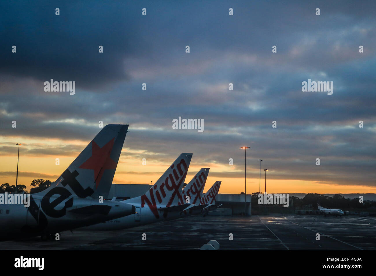 Adelaide, Australia. 19 August 2018.  Jet Star and Virgin airplane tail fins are silhouetted against a dramatic sky during colourful sunrise at Adelaide International Airport Australia Stock Photo