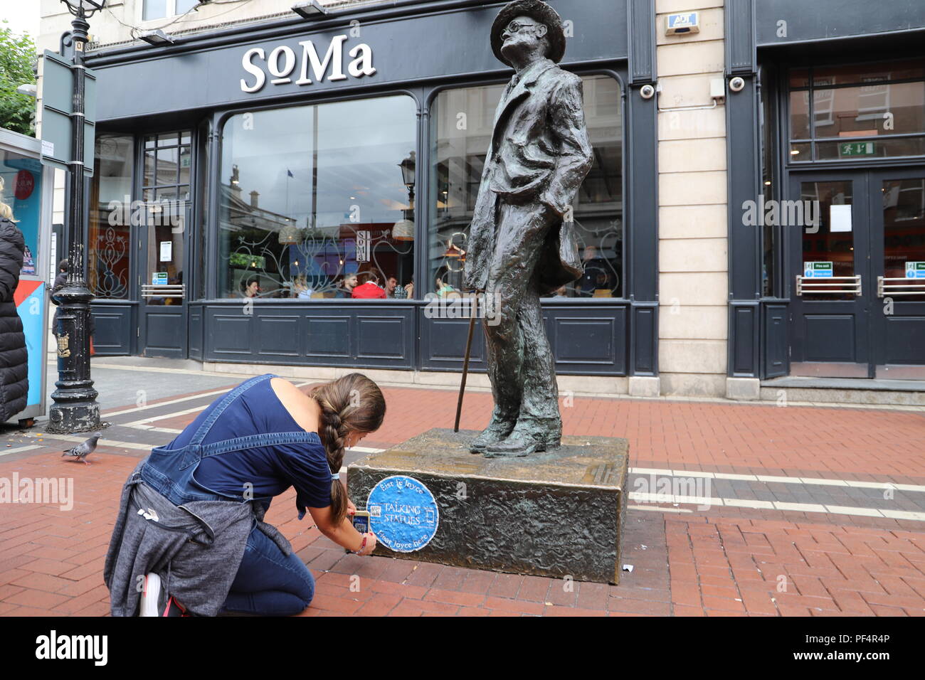 Dublin. 19th Aug, 2018. A woman scans the QR Code at the bottom of a statue of James Joyce, a famous Irish novelist in downtown Dublin, Ireland, Aug. 18, 2018. The Irish tourism department has recently launched a 'Talking Statue' initiative in Dublin, under which people can use smart phones to listen to the talks of 11 famous statues in the city by scanning the QR Codes attached to them. Credit: Xinhua/Alamy Live News Stock Photo