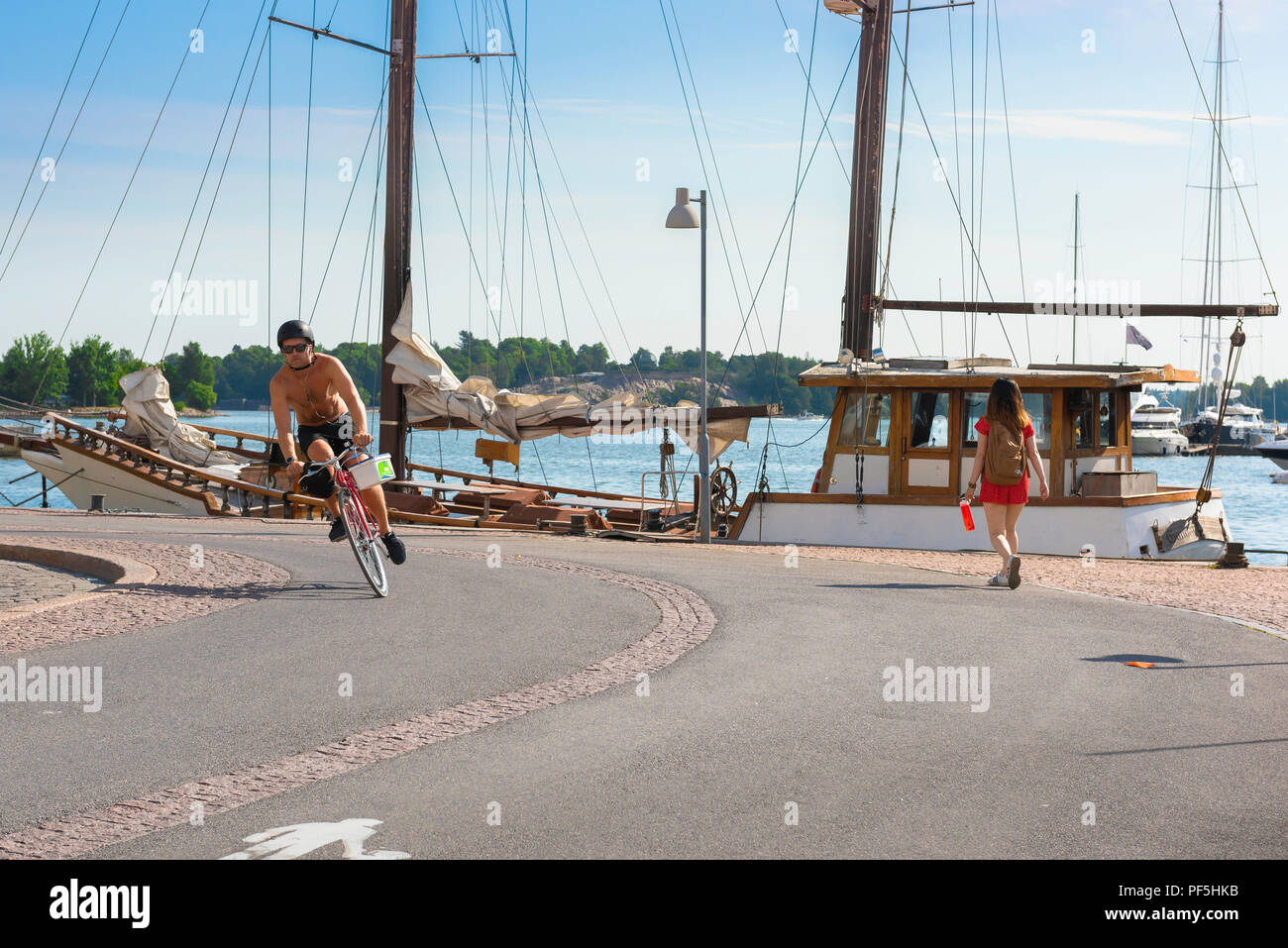 Helsinki Finland summer, view on a summer morning of a young man on a bike cycling on a cycle path along the quayside in Helsinki harbor, Finland. Stock Photo