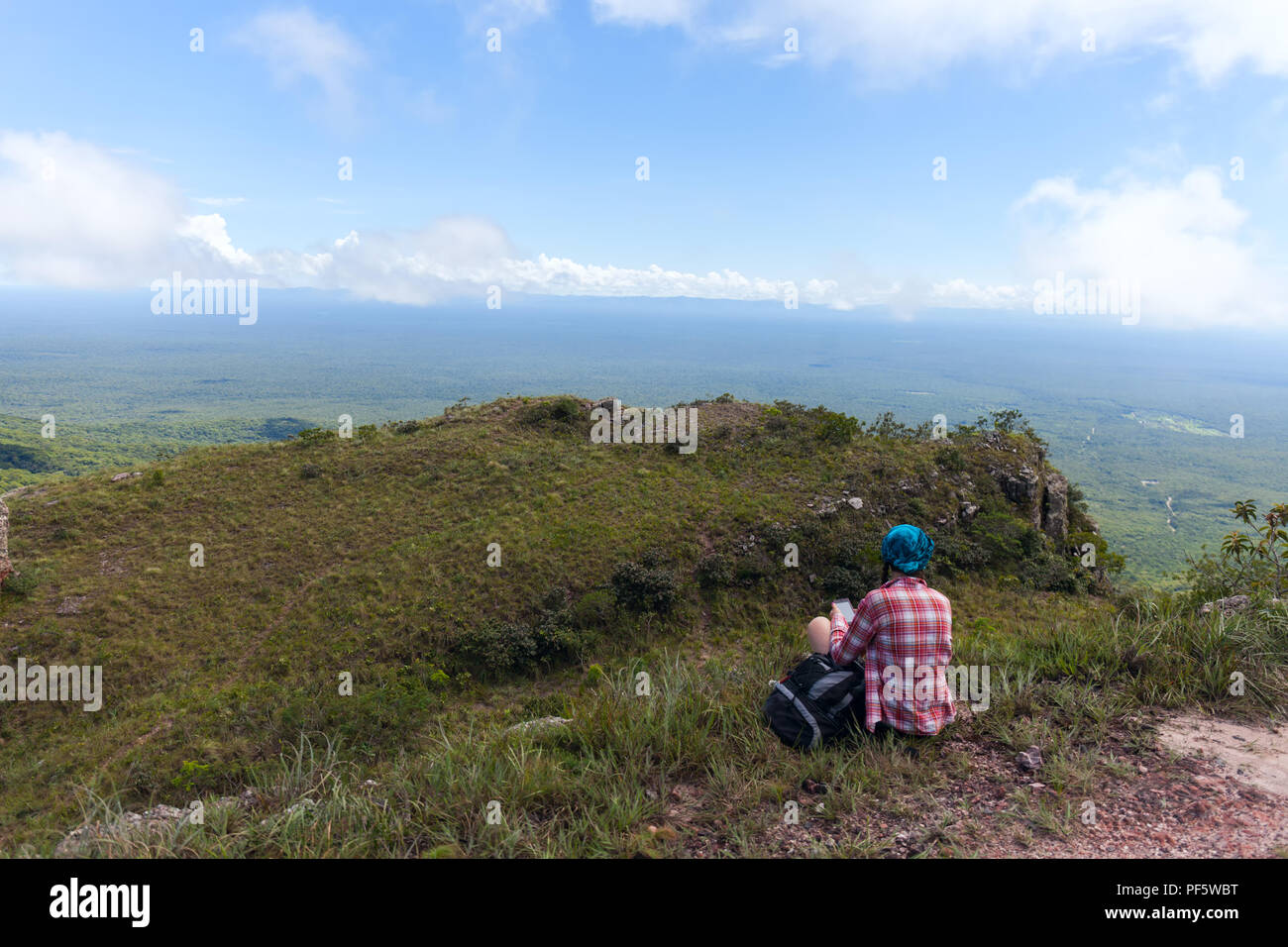 Young woman sitting on a rock with backpack and looking at here mobile phone Stock Photo