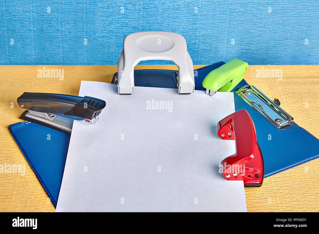 Two hole puncher and two staplers lie over office folder with a spring clip  or clipboard and the empty sheet of white paper with copy space, mockup fo  Stock Photo - Alamy