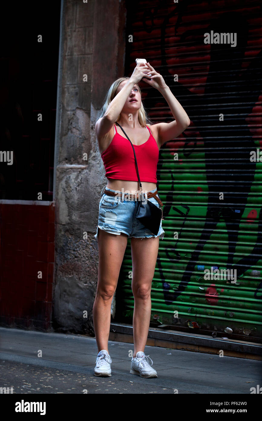 Young blonde woman taking photos using a smartphone, Gracia, Barcelona. Stock Photo