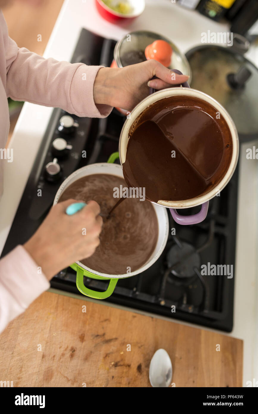 Overhead view of a cook emptying chocolate sauce from a pot pouring it into a second green pot on a stove. Stock Photo