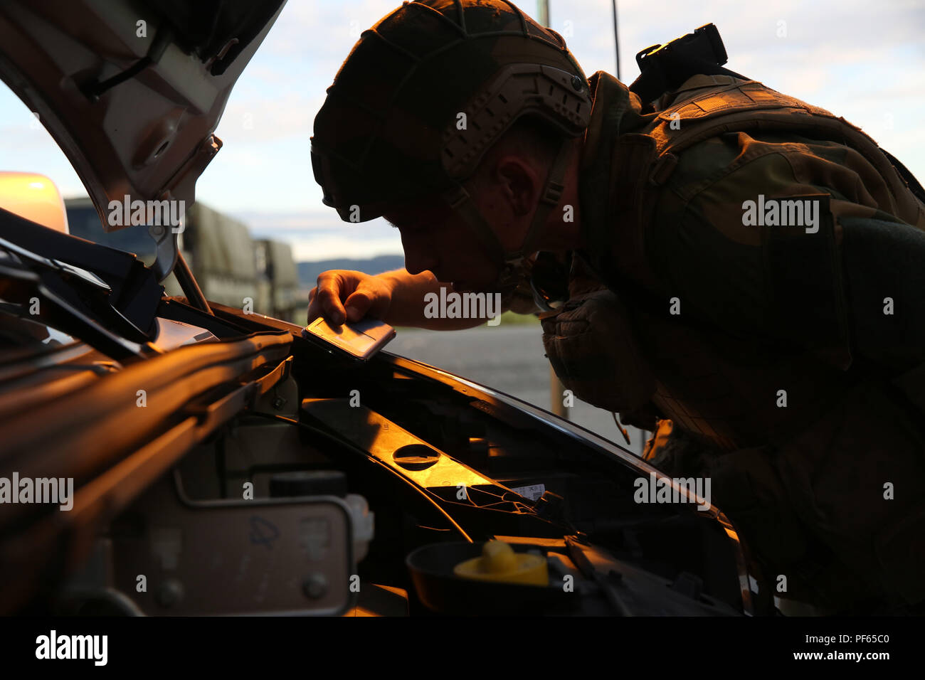 A Norwegian soldier searches for contraband under the hood of a vehicle during a multinational law enforcement exercise in Vaernes Garnison, Norway, Aug. 14, 2018. Service members practiced vehicle control and entry control point procedures used to identify and search vehicles and personnel entering a military installation. The training, conducted by U.S. Marines with Marine Rotational Force-Europe 18.1, taught American, Norwegian and British military members how to properly set up and execute the checkpoints. (U.S. Marine Corps photo by Cpl. Gloria Lepko/Released) Stock Photo
