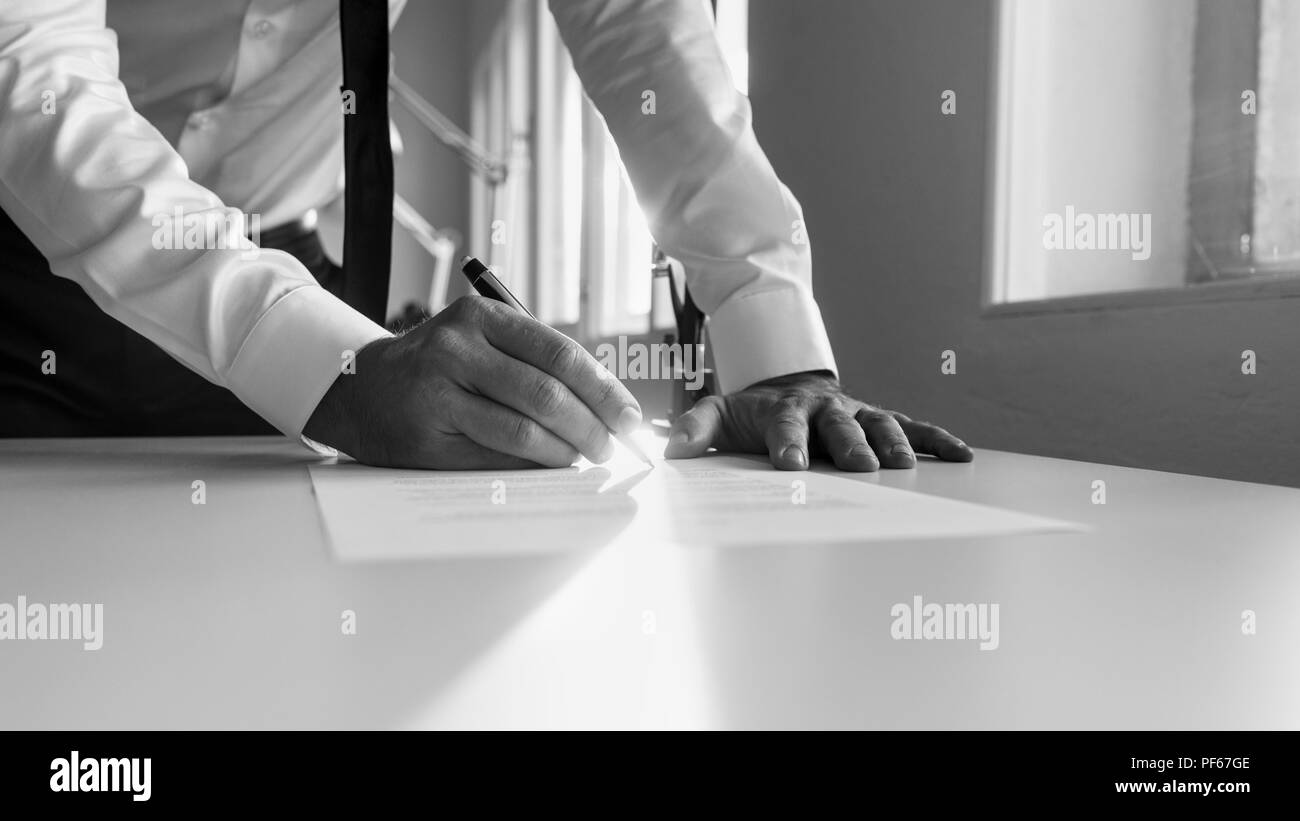 Greycale image of a man signing contract or document in the office at sunset. Stock Photo