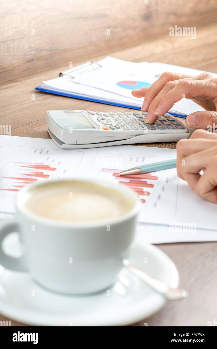 Female business accountant proofreading financial annual report presented in graphs verifying profit and earnings on white calculator. Focus on calcul Stock Photo