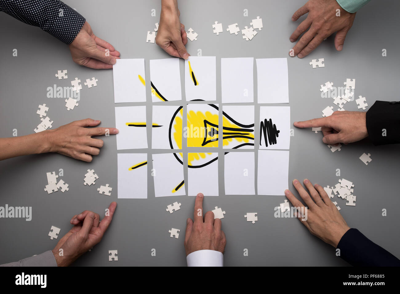 Top view of businesspeople hands touching white papers arranged on a gray table forming a yellow light bulb. Conceptual for brainstorming and teamwork Stock Photo