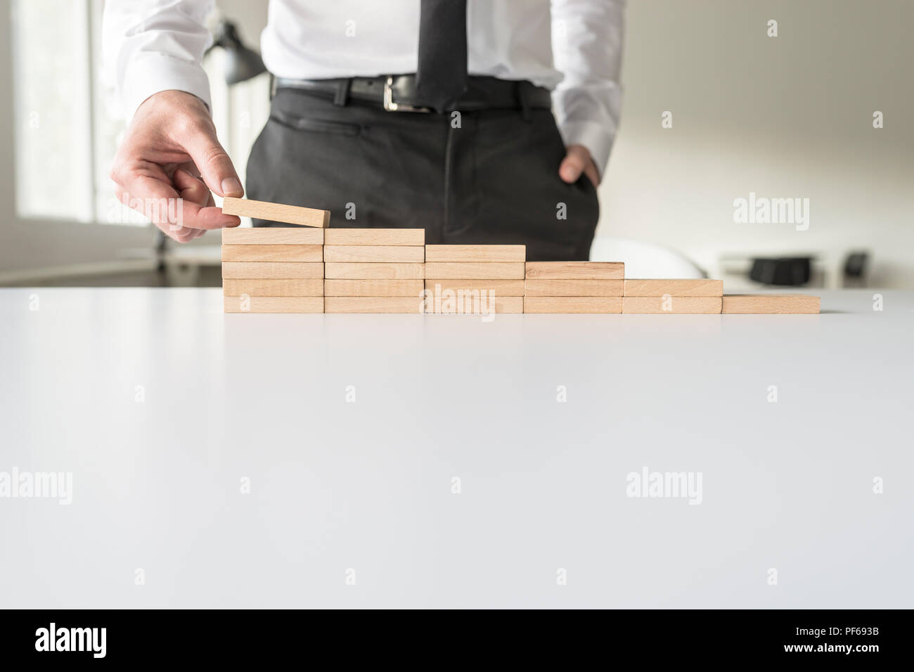 Businessman standing behind his white office desk constructing steps of