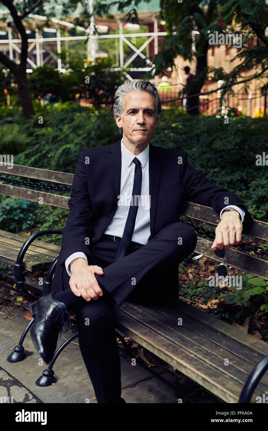 Grey Haired Man in Black Suit Sits on Park Bench Stock Photo