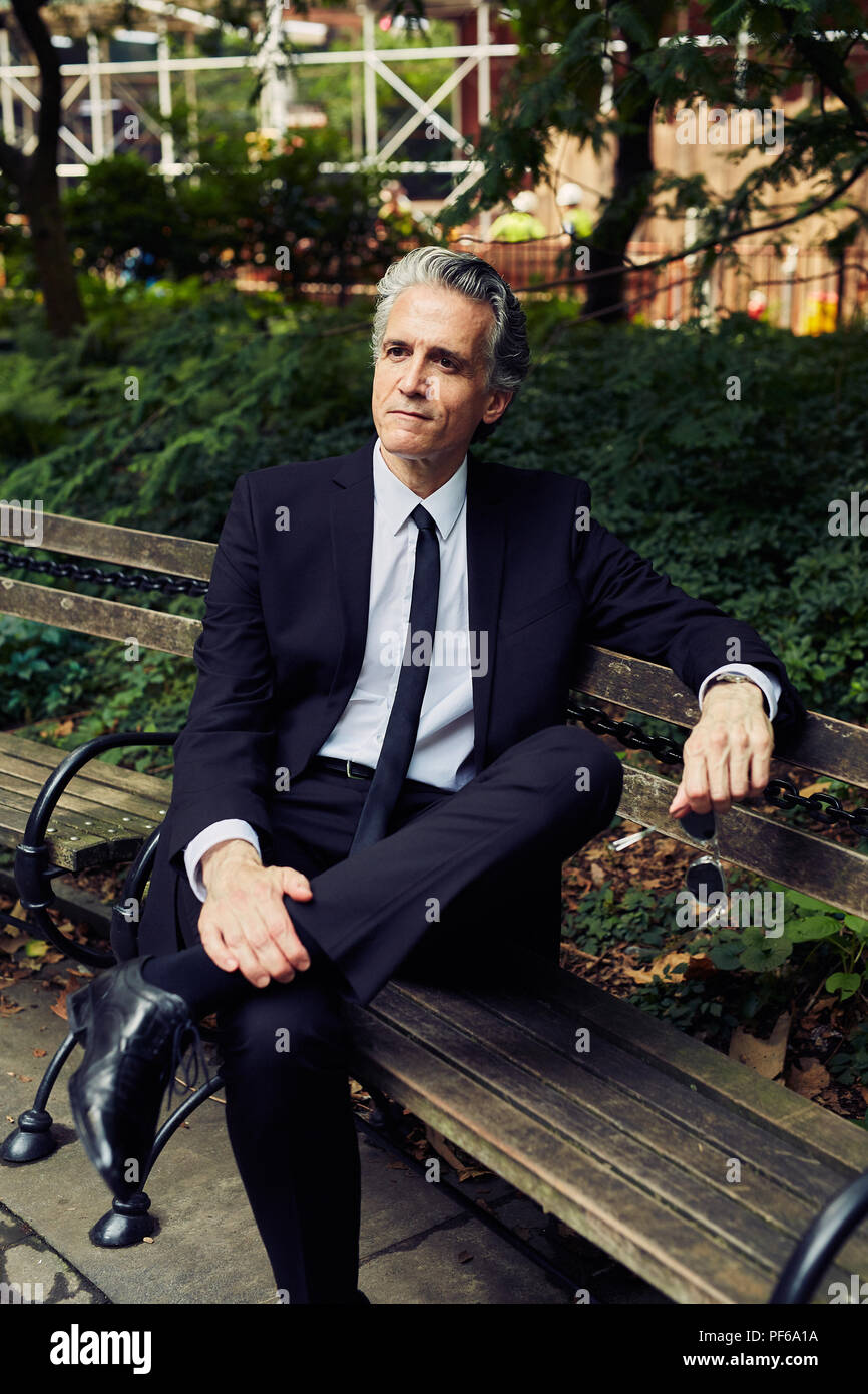 Grey Haired Man in Black Suit Sits on Park Bench Stock Photo
