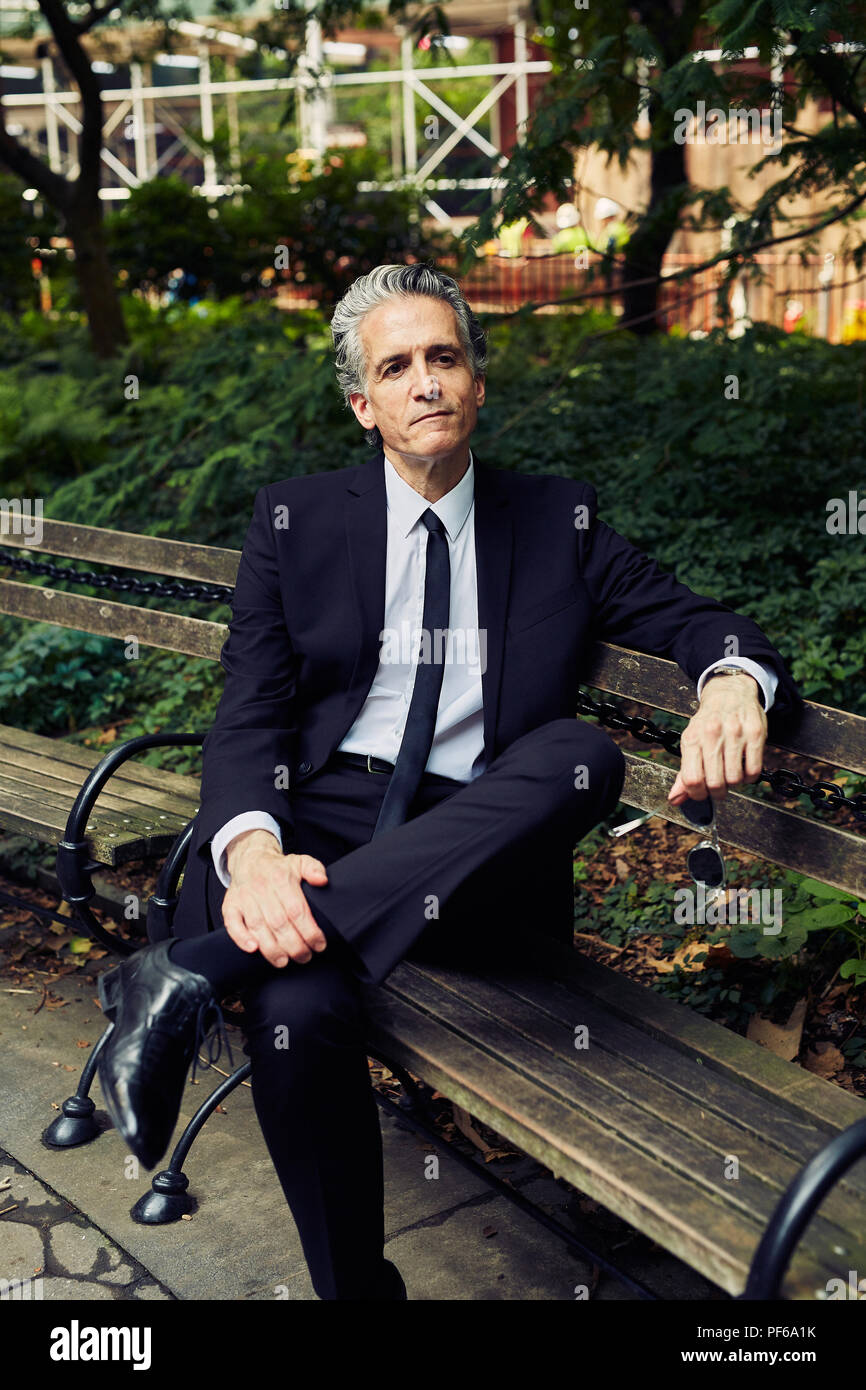 Grey Haired Man in Black Suit Sits on Park Bench Stock Photo
