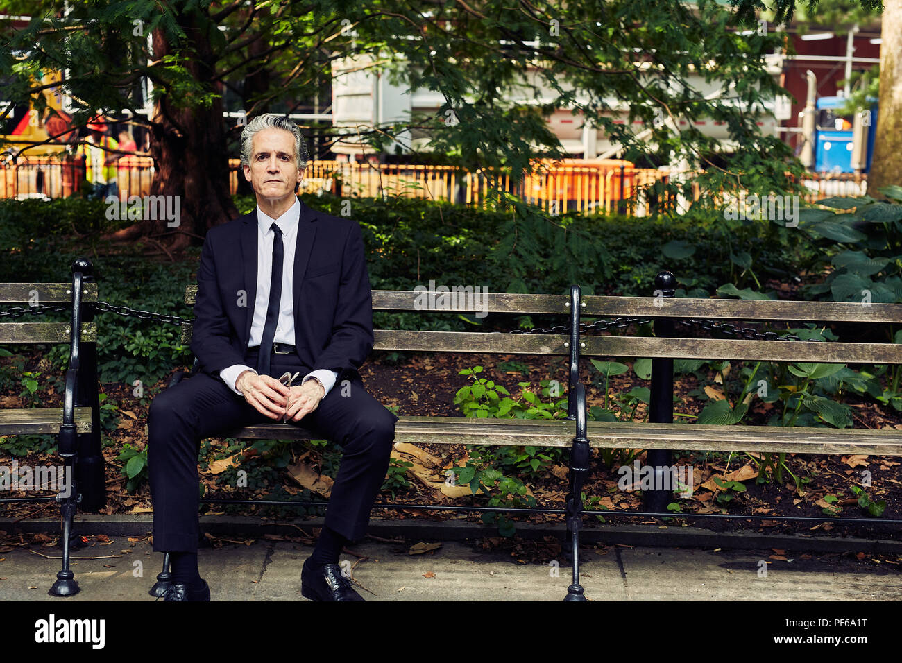 Grey Haired Man in Black Suit Sits on Park Bench Stock Photo