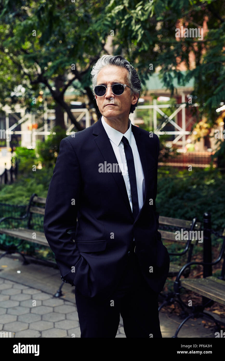 Grey Haired Man In Black Suit Walks Thru A Park Stock Photo