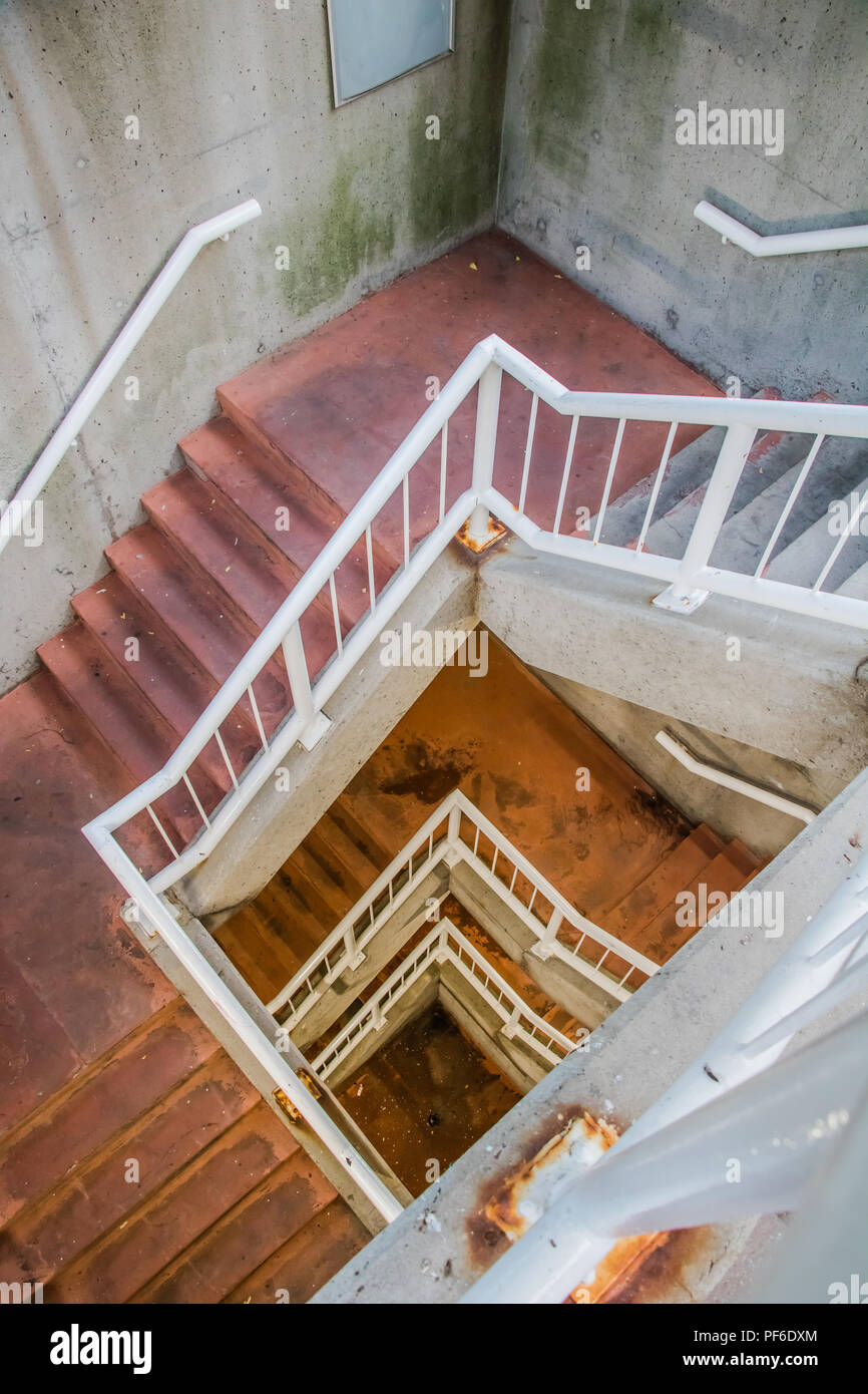 looking down dirty stair case with red flooring and white railing Stock Photo