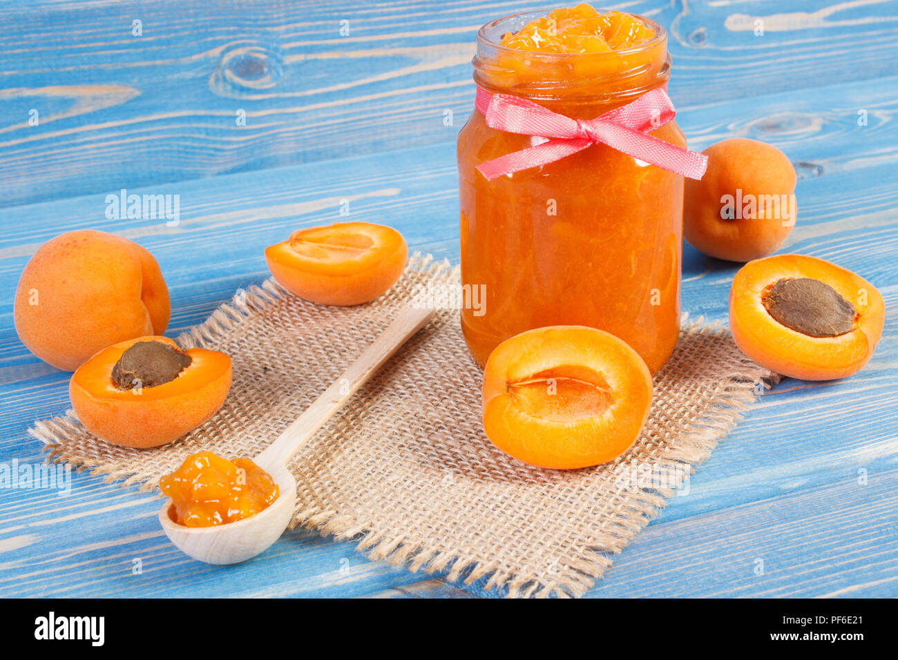 Apricot jam or marmalade in glass jar and ripe fruits on blue boards, concept of healthy sweet dessert Stock Photo