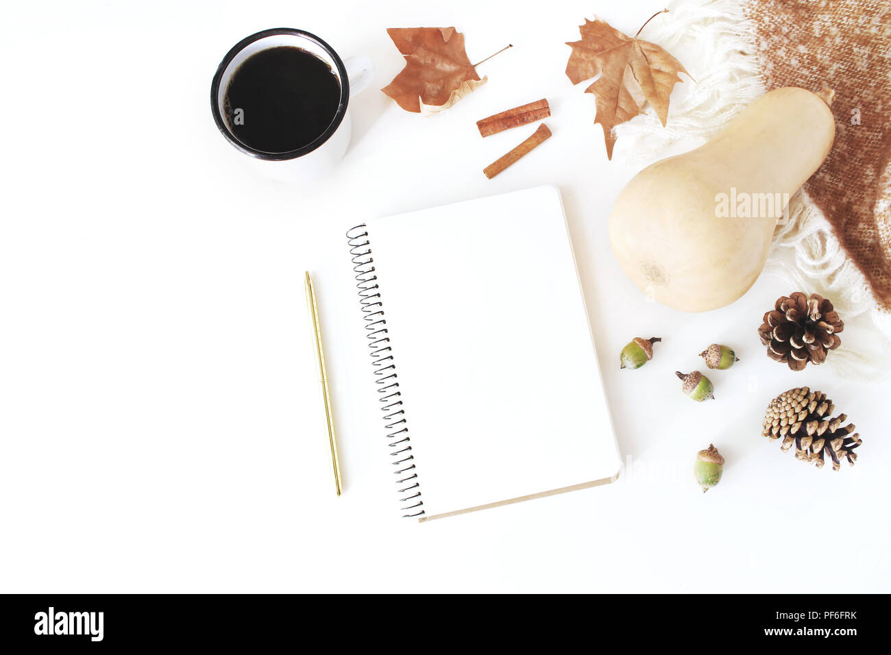 Autumn, fall workspace composition. Notebook mock-up scene. Cup of coffee, wool blanket, autumn leaves, cinnamon sticks, pine cones, acorns and pumpki Stock Photo