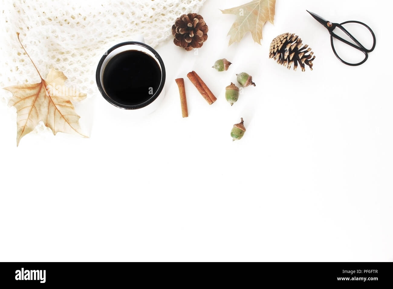 Autumn, fall composition. Cup of coffee, knitted blanket. Autumn leaves and cinnamon sticks. Pine cones, acorns and vintage scissors. White table back Stock Photo