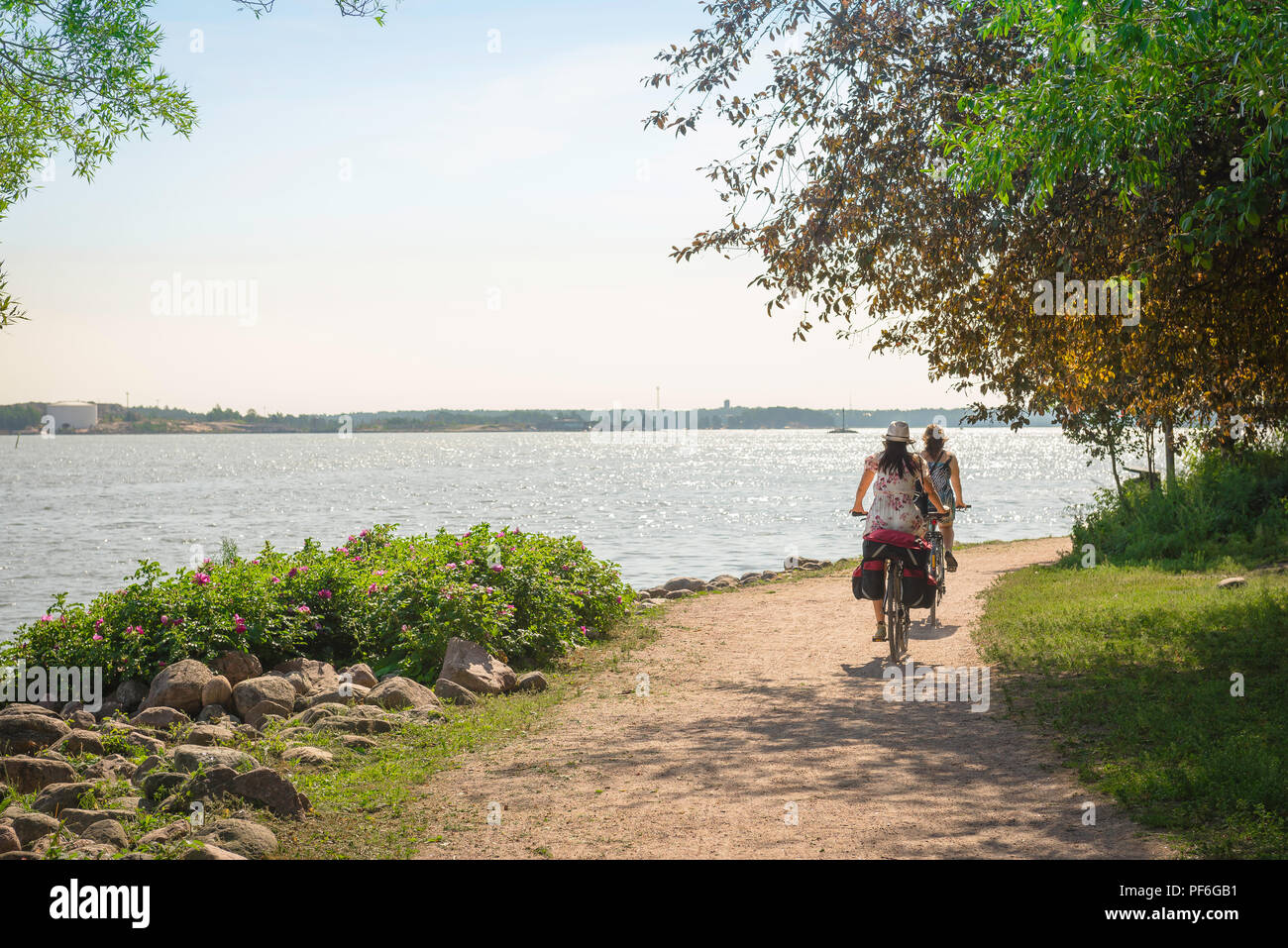 Helsinki island summer, view on a summer morning of two young women riding on a cycle path on Katajanokka Island near Helsinki, Finland. Stock Photo