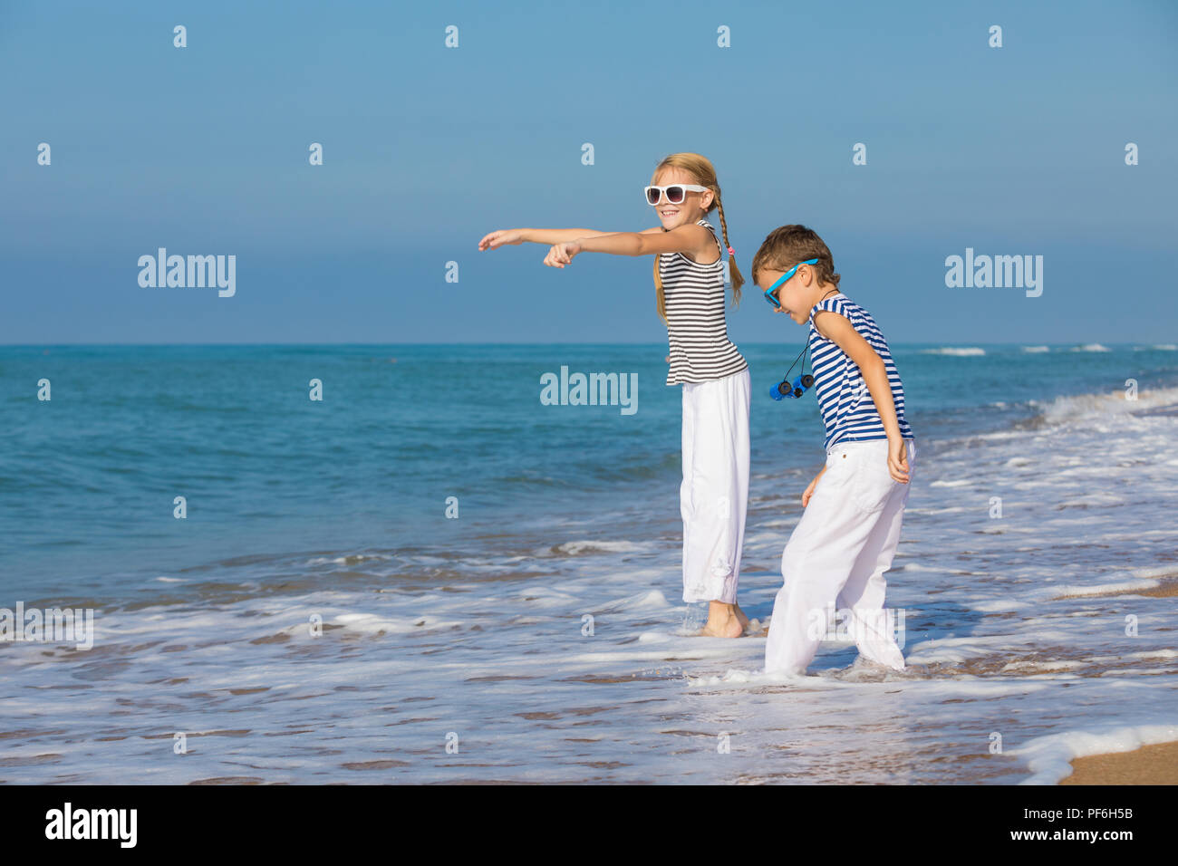 Two happy little children playing on the beach at the day time. They are dressed in sailor's vests. Kids having fun outdoors. Concept of sailors on va Stock Photo