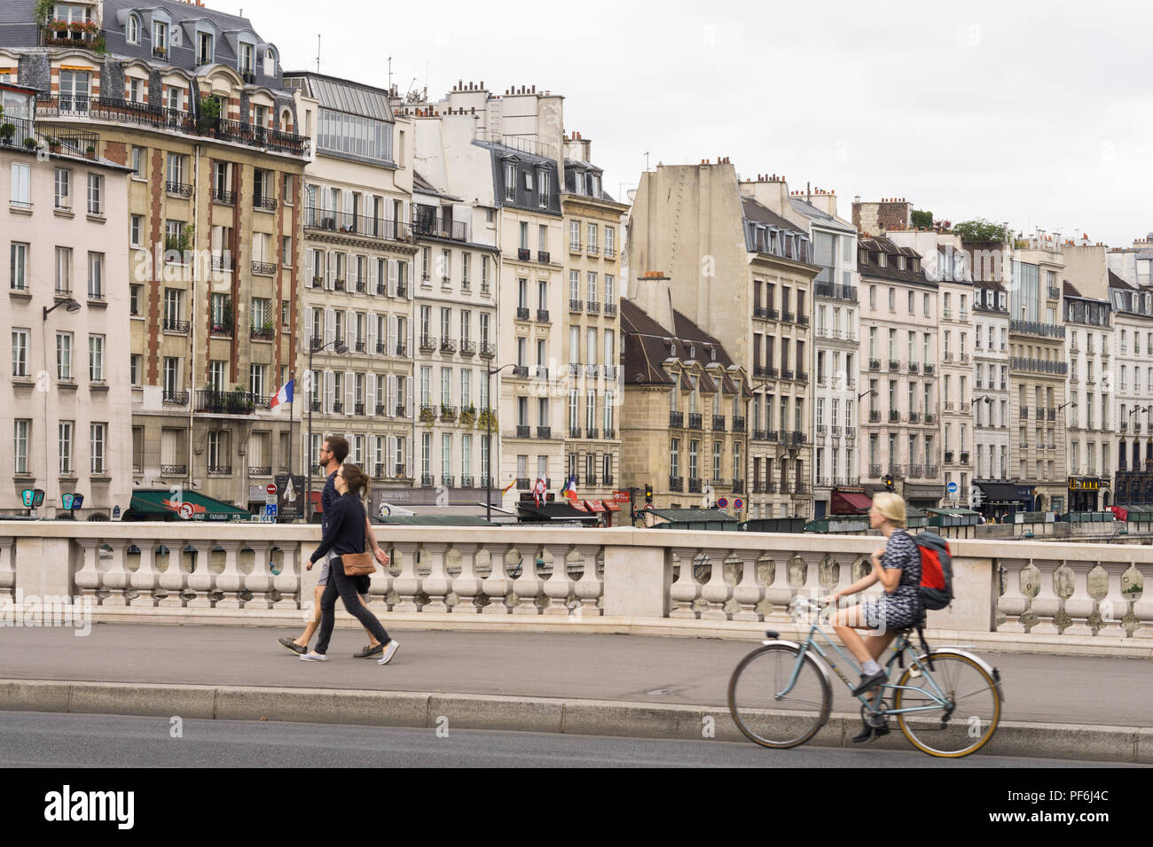 Paris cityscape - Woman cycling over the Saint Michel bridge, buildings on Quai des Grands Augustins are in the background. Paris, France, Europe. Stock Photo