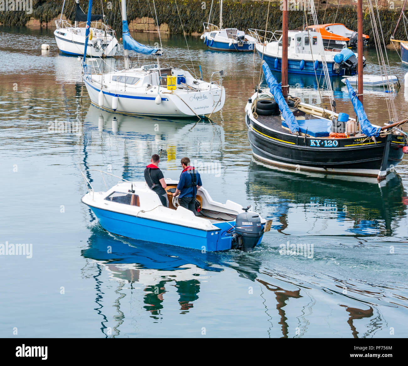 Dunbar, East Lothian, Scotland, United Kingdom, 20th August 2018. UK Sunshine in Dunbar harbour. Two men leave the harbour in a small boat with moored boats including fishing boats and yachts Stock Photo