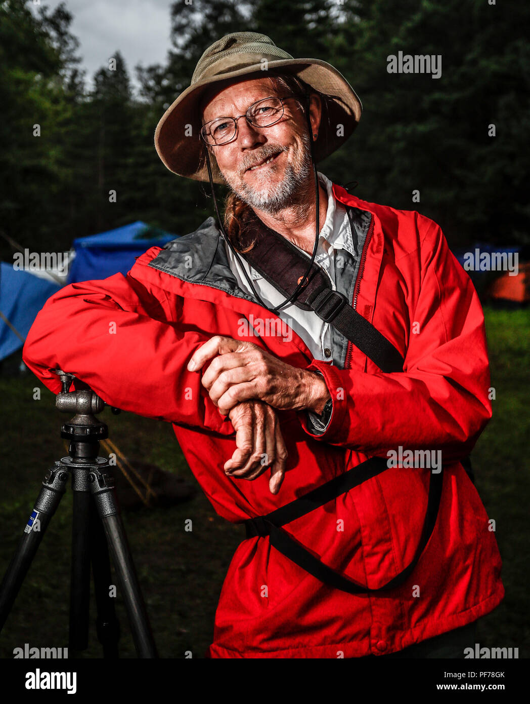 retrato del fotografo y biologo Chip Hedgcock recargado en su tripie. viste de sombrero, usa lentes e impermiable color rojo.    portrait of the photographer and biologist Chip Hedgcock recharged in his tripie. wear a hat, wear glasses and an impervious red color.  https://www.charleshedgcock.com  Charles 'Chip' Hedgcock has combined his love of the outdoors with more than 25 years of experience photographing in medicine, the life sciences, and fine arts, to create a unique vision of the natural world. Whether he is chasing fringe-toed lizards over remote sand dunes in the summer heat or, ligh Stock Photo