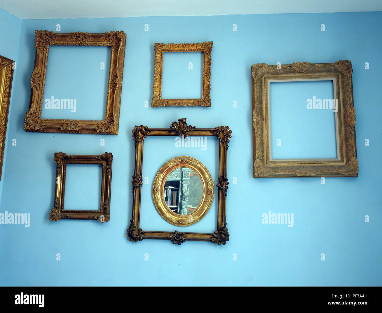 Large collection of Gilt Gold picture frames with no pictures in the frames  hanging on walls with plain background. Property released Stock Photo