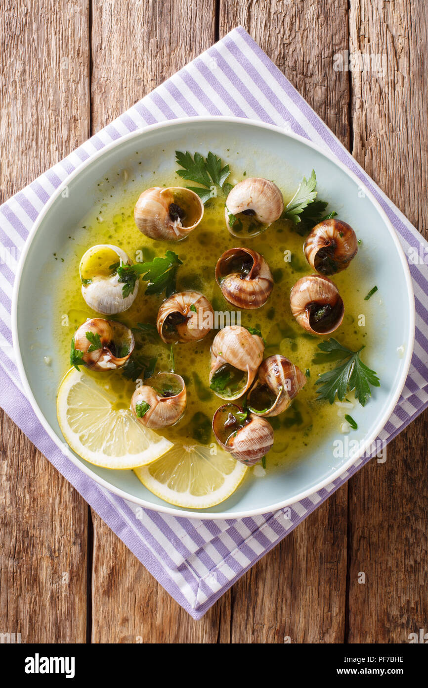Cooked French snails, escalgot with butter, herbs, lemon and garlic closeup on a plate on the
