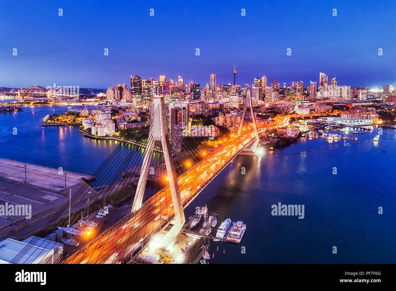 Bright cable Anzac bridge over Sydney harbour leading to city CBD illuminated at sunset under dark blue sky in Australia. Stock Photo