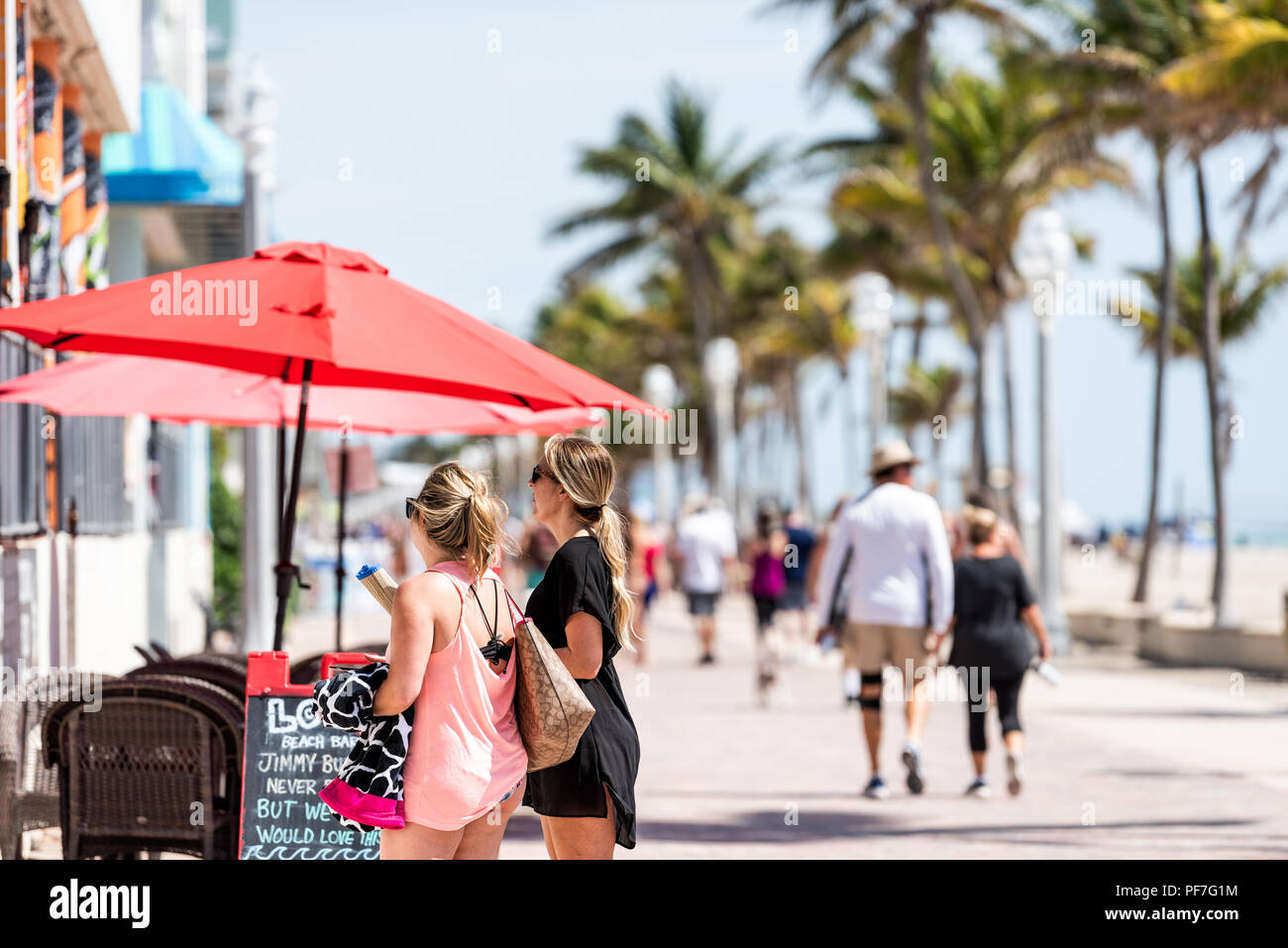 Hollywood, USA - May 6, 2018: Beach boardwalk in Florida, Miami Broward area with sunny day, young women looking at restaurant, people walking on coas Stock Photo