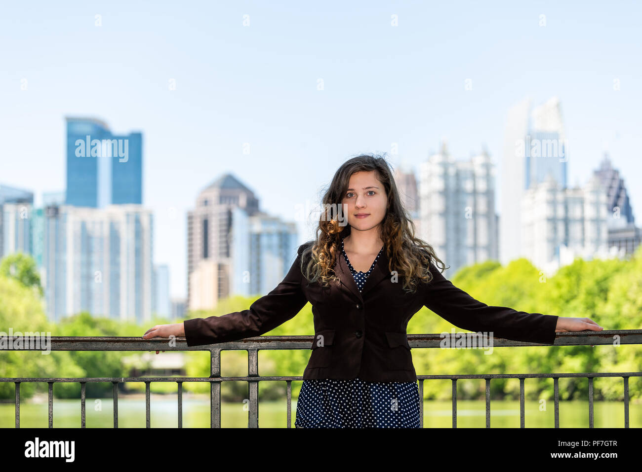 Young woman realtor face standing in Piedmont Park in Atlanta, Georgia scenic water, and cityscape skyline of urban city skyscrapers downtown, Lake Cl Stock Photo