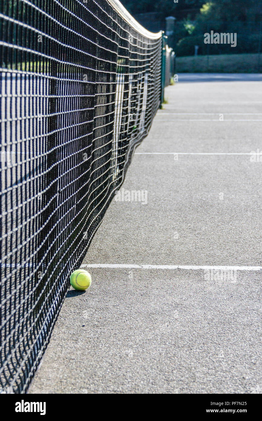 Low angle shot of of a yellow tennis ball on the ground next to the net